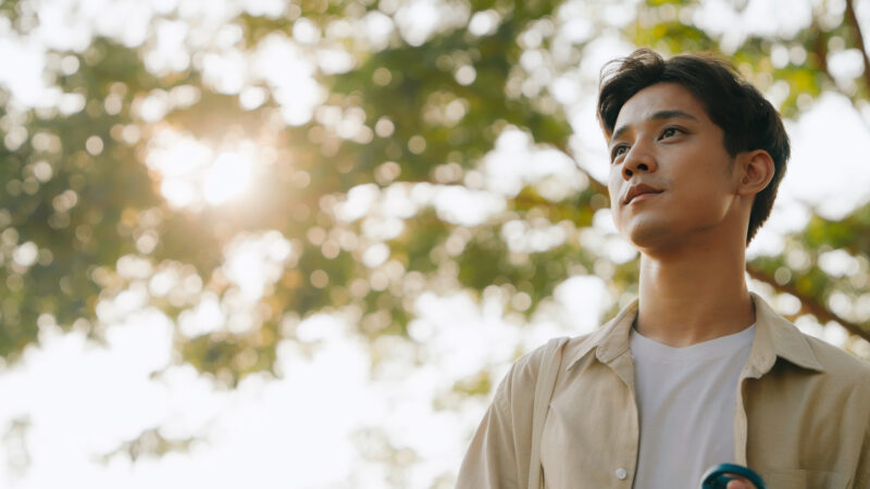 Young man standing outside in nature with a reflective expression, representing self-awareness and the journey toward understanding alcohol abuse treatment options.