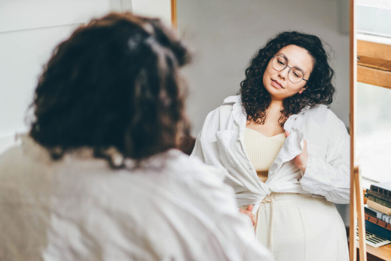 Woman examining her reflection in the mirror, illustrating a common body checking behavior linked to body image concerns.