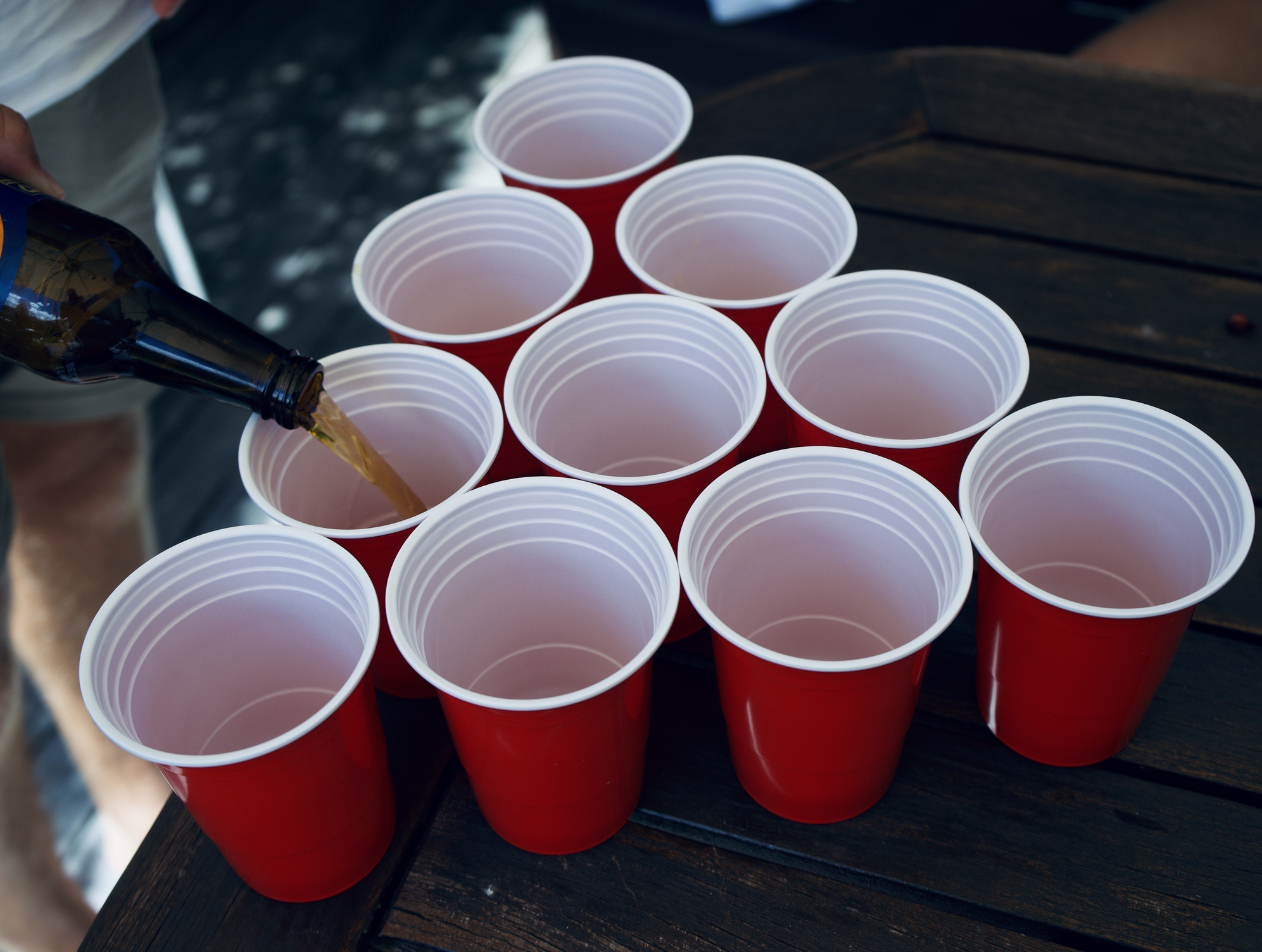 Alcohol being poured into red solo cups on a table, symbolizing binge drinking culture and early signs of alcohol use disorder, especially among young adults.
