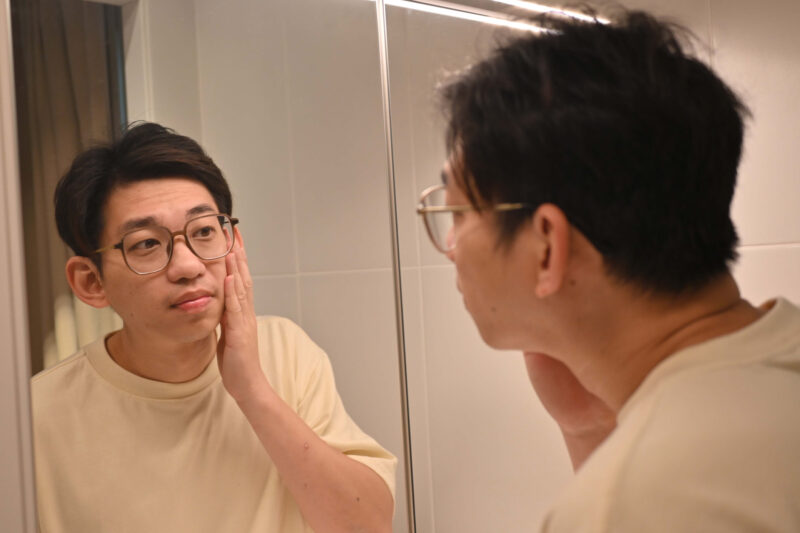 Man touching his face while looking in the mirror, symbolizing the self-scrutiny often associated with body dysmorphia and gender dysphoria.