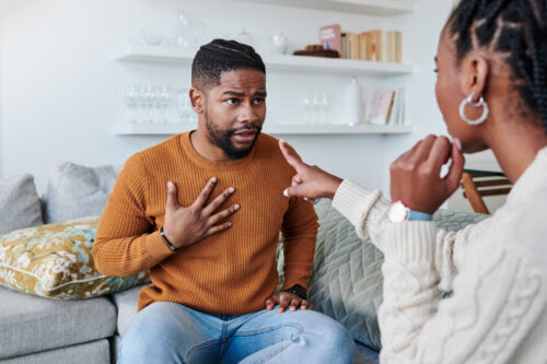 Man holding his chest and looking concerned while a woman points at him during an intense conversation. The image captures the tension and confusion that can arise when being accused of narcissistic behavior or trying to defend oneself.