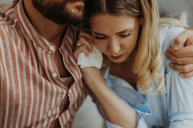 Close-up of a woman holding a tissue and leaning into someone’s shoulder, showing visible emotional vulnerability. The image captures the complexity of seeking comfort while struggling with emotional closeness and trust.