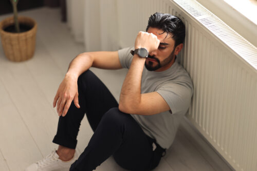 Man sitting on the floor with eyes closed and arm resting over his face, appearing emotionally overwhelmed. The image reflects deep psychological distress, capturing the isolation and disorientation that can accompany trauma-induced psychosis.