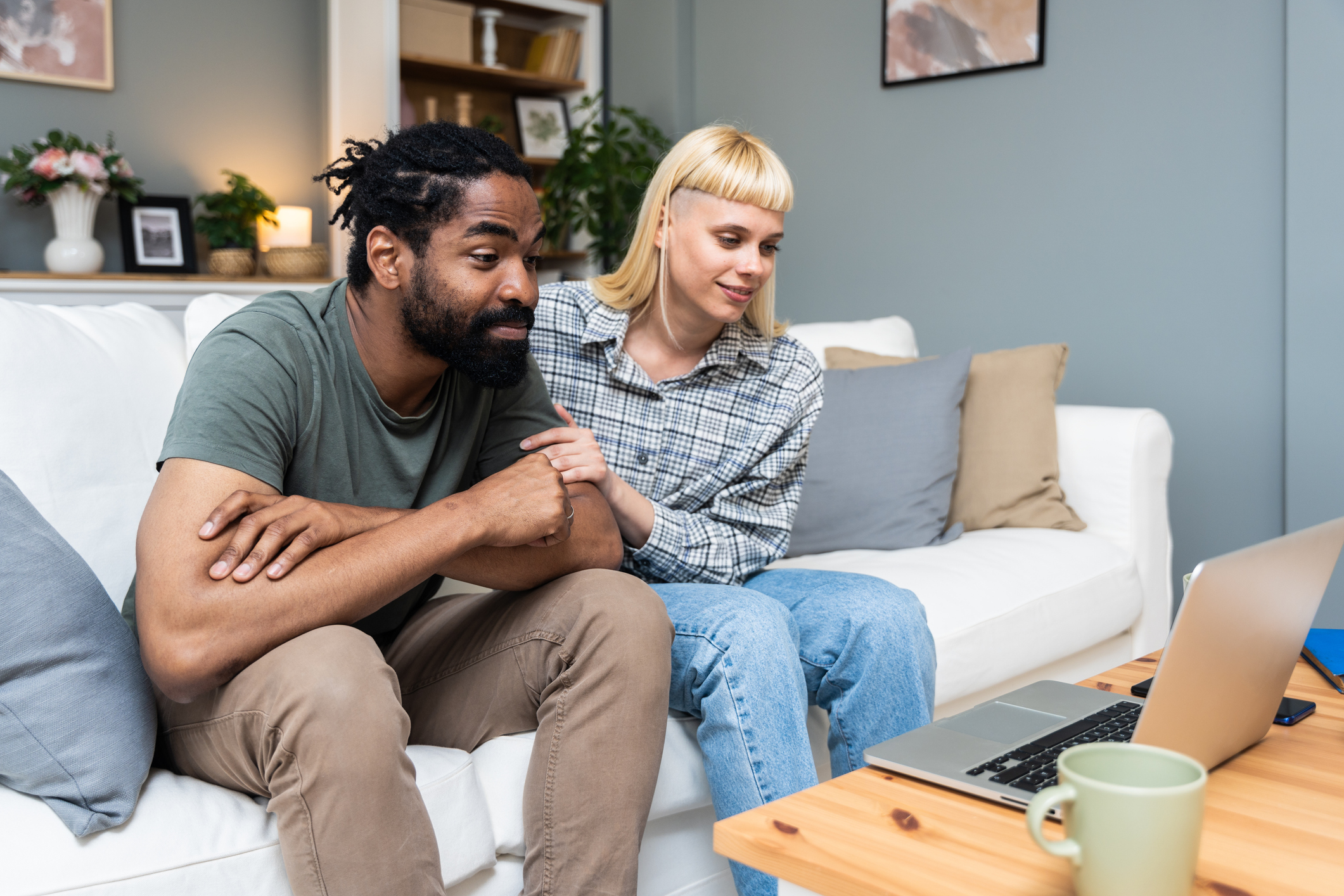 Two people sitting close together on a couch, watching something on a laptop and sharing a moment of connection. The image reflects healthy communication and mutual support—key elements in overcoming self-sabotaging relationship habits.