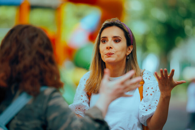 Two people in conversation outdoors, with one person appearing frustrated or defensive while gesturing with their hands. The image suggests emotional tension or miscommunication, reflecting the dynamics often present in a toxic friendship.