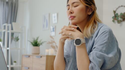 Person sitting with eyes closed and hands clasped, appearing deep in thought or emotionally overwhelmed. The image conveys a moment of inner reflection or emotional processing, often linked to trauma-related behaviors like oversharing.
