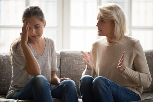 A distressed young woman holds her head in her hand while an older woman speaks to her, representing the conflict and emotional strain of narcissistic abuse.