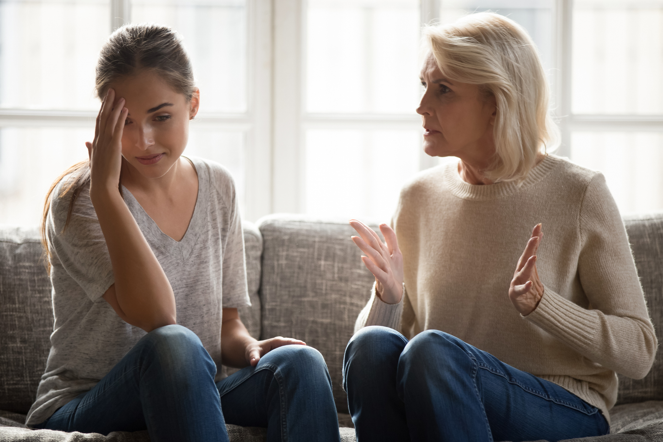 A distressed young woman holds her head in her hand while an older woman speaks to her, representing the conflict and emotional strain of narcissistic abuse.