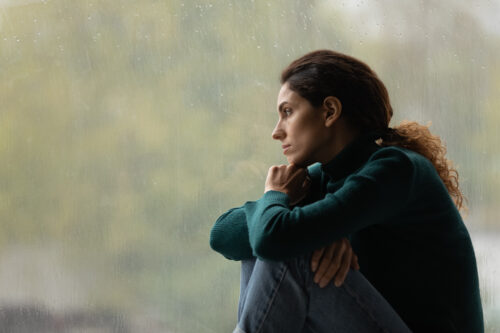 A woman sits by a rainy window, deep in thought, symbolizing the sadness and reflection tied to reactive depression.