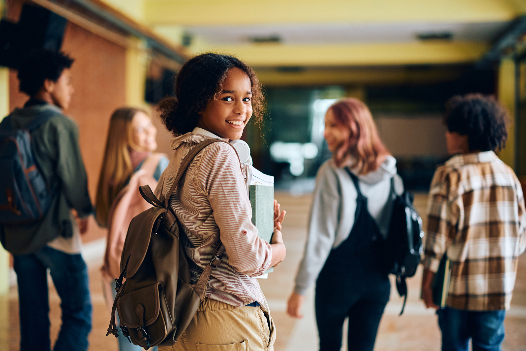 A student smiles while holding books in a school hallway, representing the excitement and challenges of returning to school.