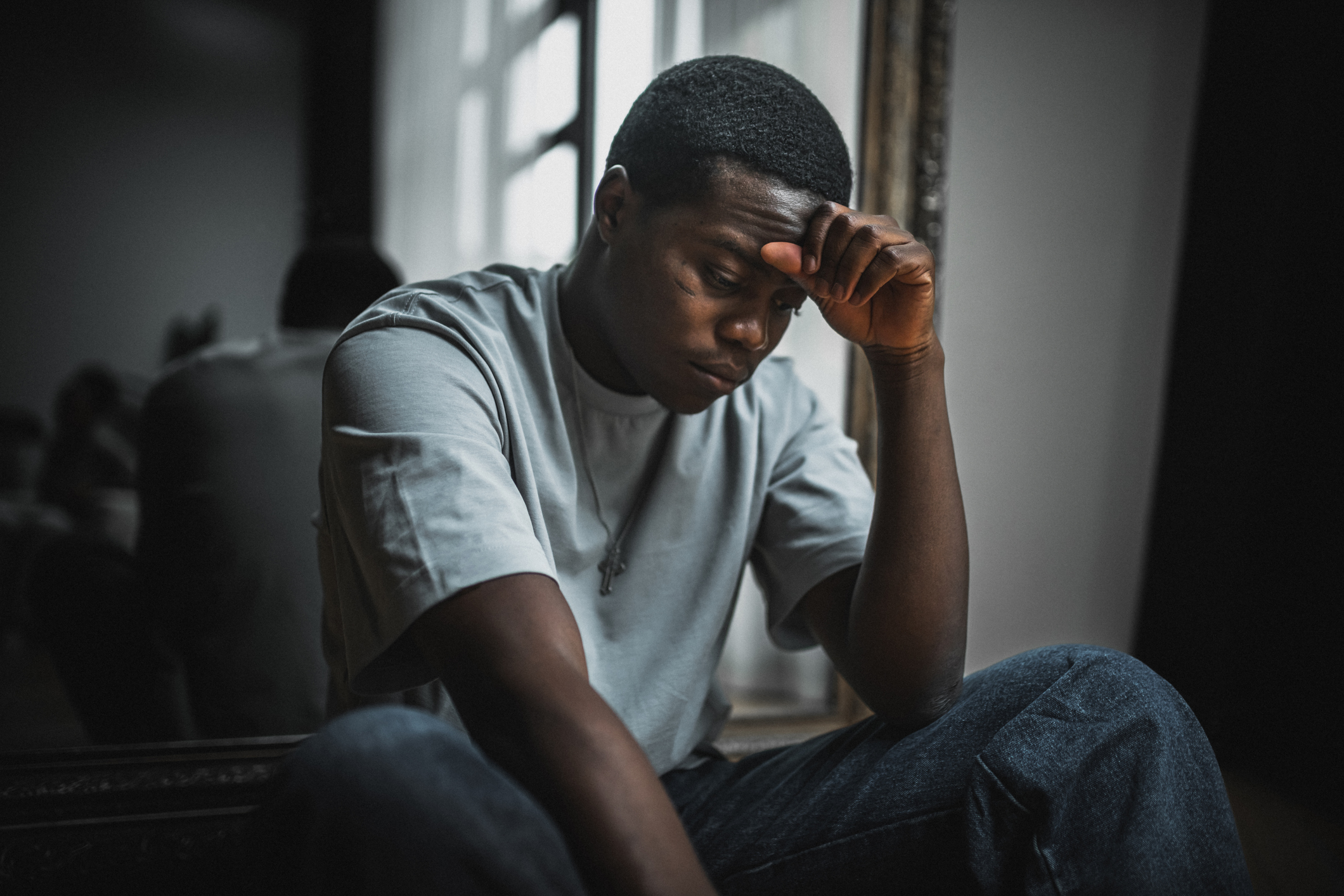 Young Black man sitting by a window with his head resting on his hand, looking overwhelmed or stressed. This image reflects the emotional weight of high cortisol levels and the connection to anxiety, as explained by therapists.