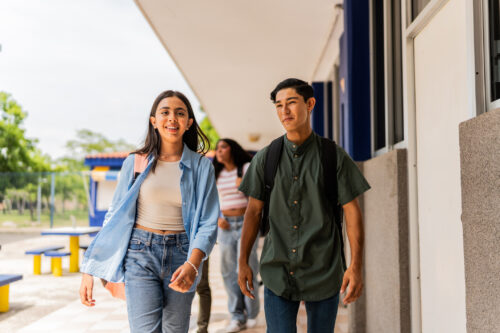Two high school students walk side by side on campus, smiling as they head to class, symbolizing the back-to-school season.