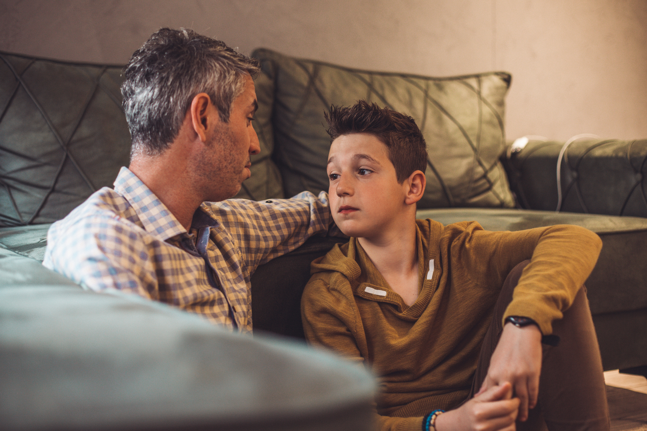 A teen sitting on a couch with arms folded, listening with a serious expression during a conversation — illustrating the importance of recognizing and addressing behavioral concerns early.
