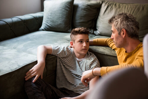 An adult and child sitting close together on the floor, having a heartfelt conversation about a difficult topic.