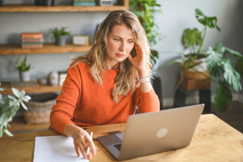 A tired teacher working on a laptop at home, holding her head in stress, symbolizing teacher burnout and exhaustion.