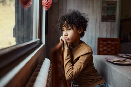 Child sitting by window with a pensive expression, illustrating childhood depression and need for therapist support.