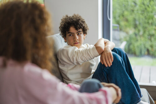 An adult and child sitting together on a couch, making eye contact during a serious conversation — representing supportive communication as a key part of addressing behavior problems.