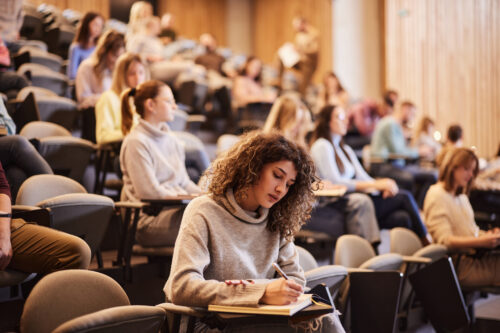 College student taking notes in a lecture hall, symbolizing academic pressure and anxiety among college students.