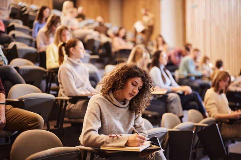 College student taking notes in a lecture hall, symbolizing academic pressure and anxiety among college students.