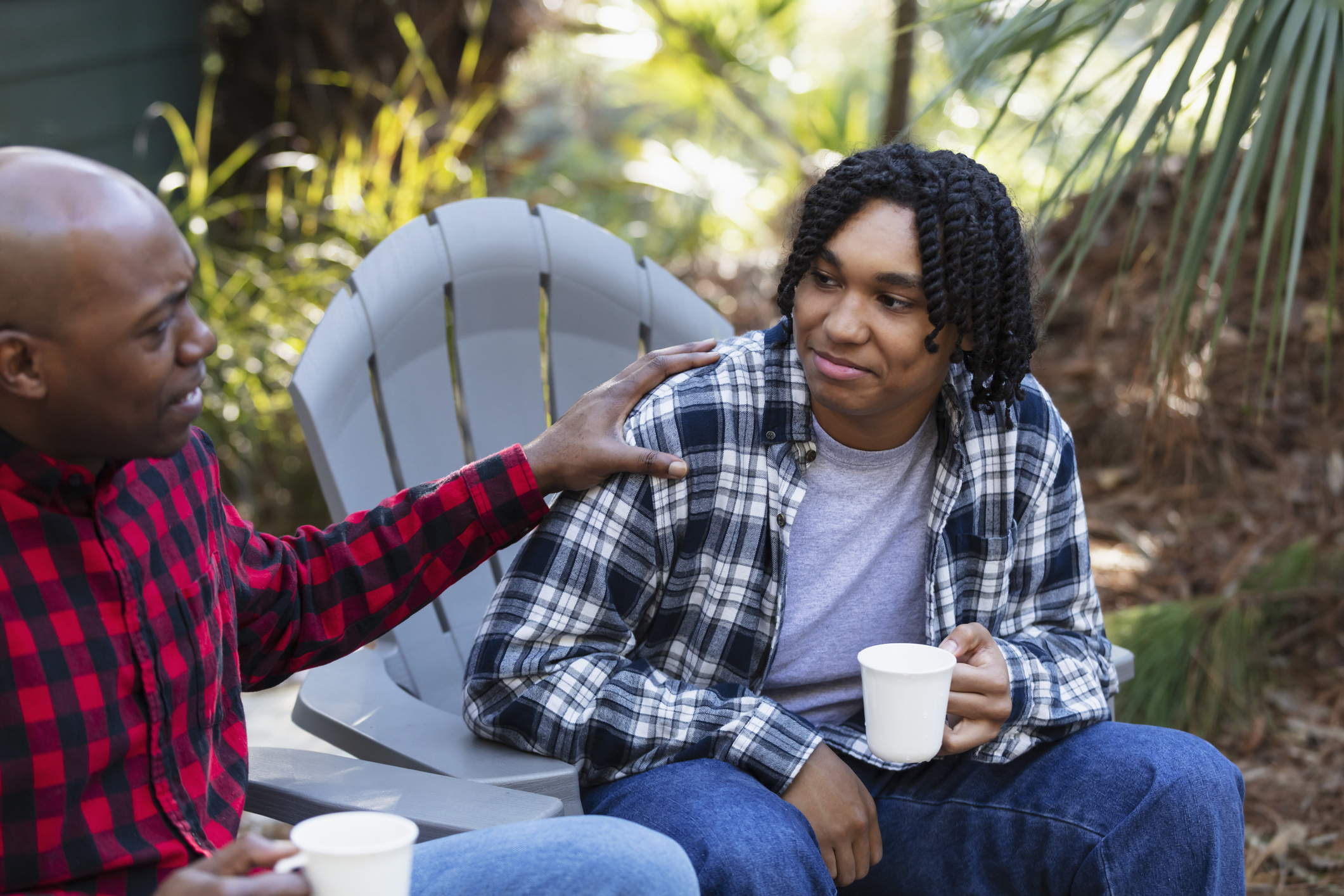 An adult gently talking with a teen outdoors, offering comfort and support during a serious conversation.