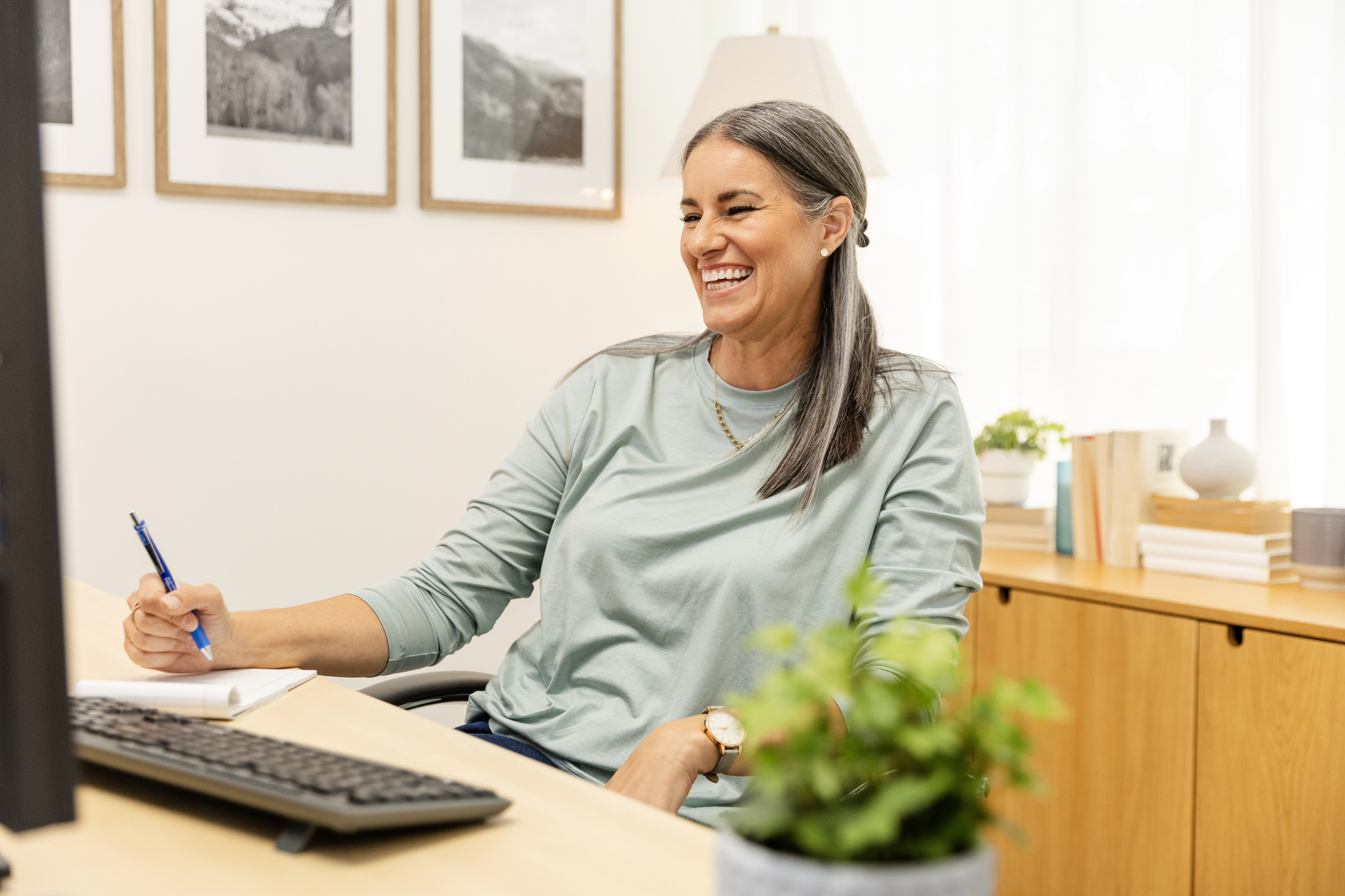 A smiling therapist sitting at a desk with a pen and notepad, engaged in an online session — representing effective therapy documentation practices.