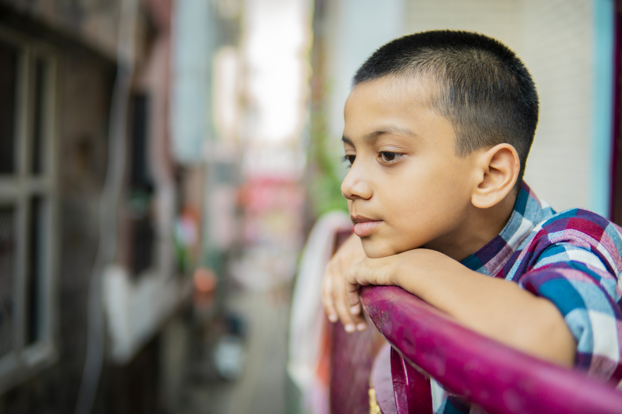 Young boy leaning on railing outdoors, appearing withdrawn and contemplative, symbolizing child depression and emotional struggles.