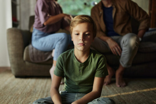Sad young boy sitting in front of parents during conflict, illustrating the emotional impact of divorce on children.