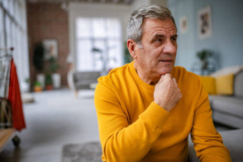 Older man in yellow sweater sitting thoughtfully at home, representing exploration of different types of narcissism.
