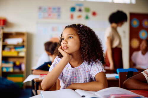 Young girl sitting at school desk with distant expression, symbolizing childhood PTSD and need for trauma-informed support.