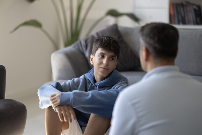 Teen sitting on the floor talking seriously with a parent at home, representing challenges of coping with a narcissistic parent.