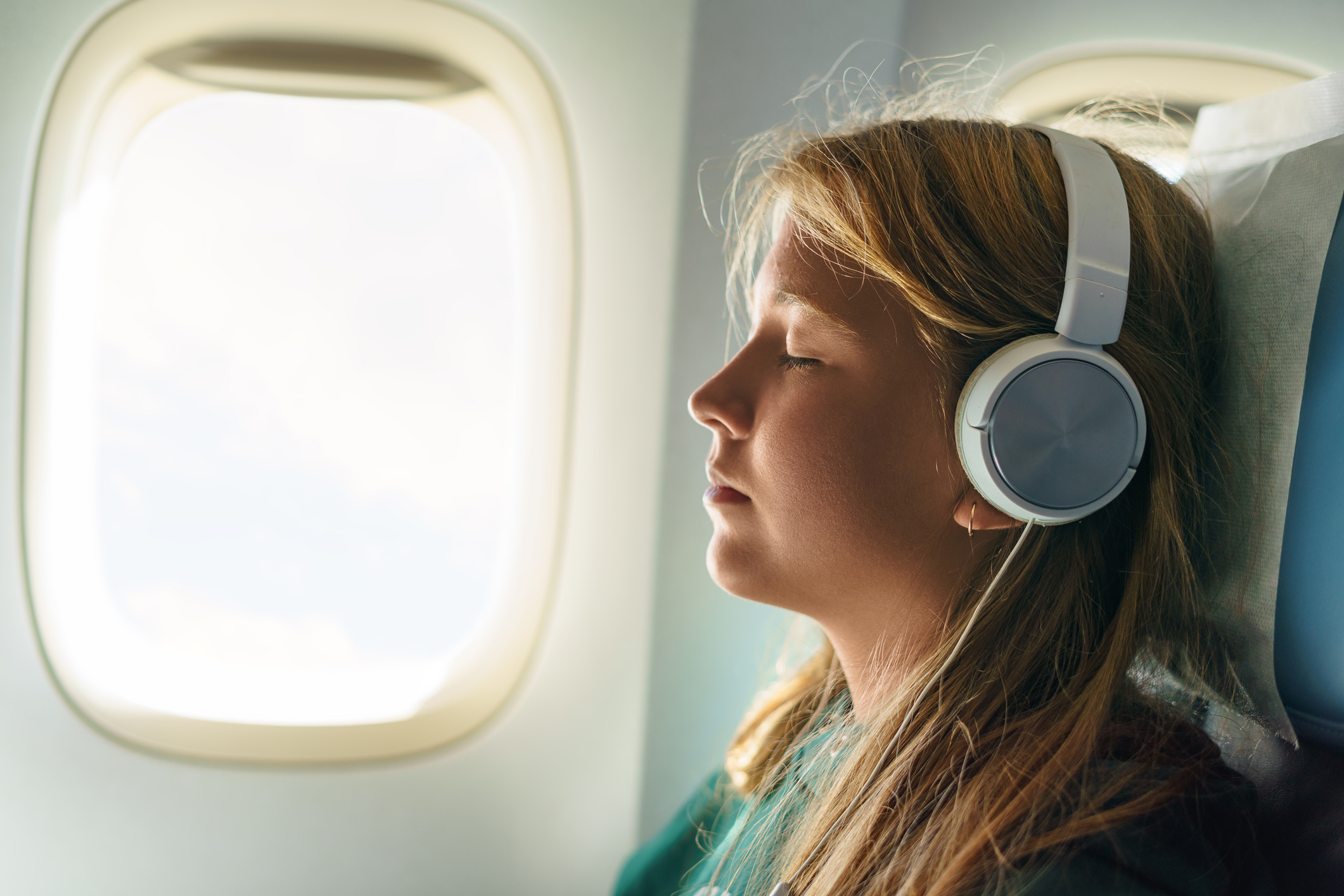 Person wearing headphones relaxing with eyes closed on an airplane, practicing calm breathing to overcome flight anxiety.