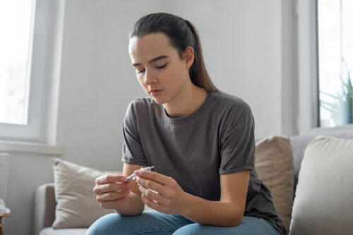 A young person sitting on a couch, looking down thoughtfully while holding a partially rolled joint, symbolizing contemplation of marijuana use and its impact on mental health.
