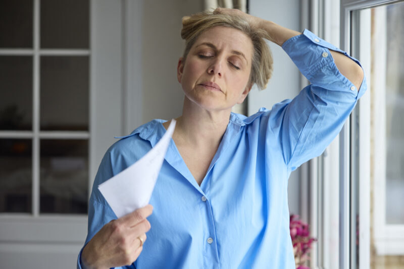 Middle-aged woman experiencing a hot flash and fanning herself, representing physical symptoms linked to menopause and depression.