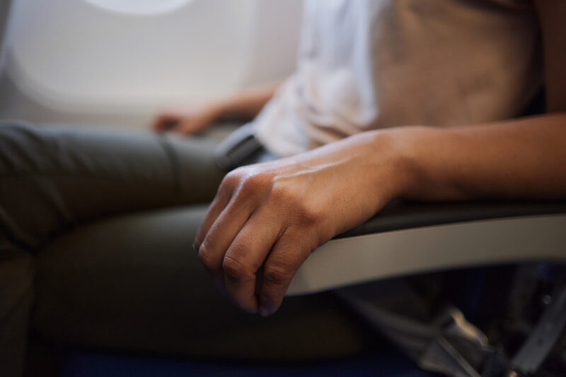 Close-up of a passenger gripping an airplane armrest during turbulence, showing signs of flight anxiety.