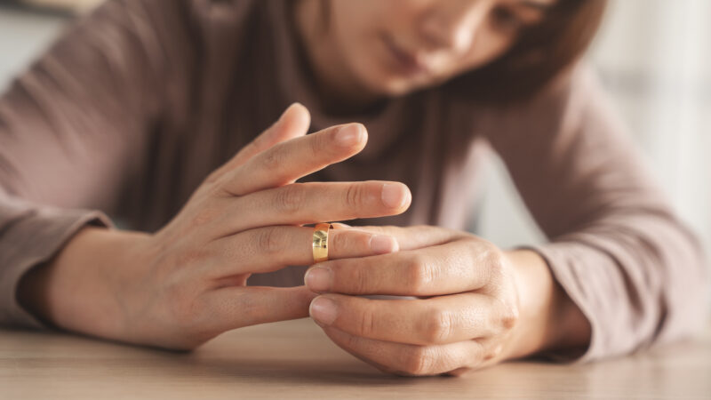 Close-up of a person sitting at a table, thoughtfully sliding a gold wedding ring off their finger, symbolizing emotional reflection and post-wedding transition.