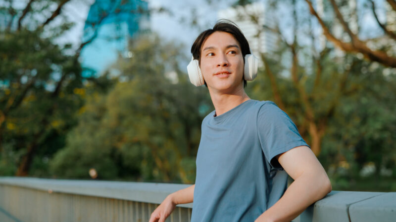 Person wearing headphones and smiling while standing outside, representing mindfulness and self-care through music and time in nature.