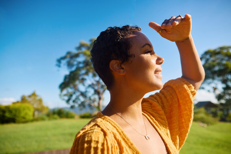 Person smiling and shading their eyes from the sun, representing resilience, self-awareness, and hope in managing bipolar dissociation.