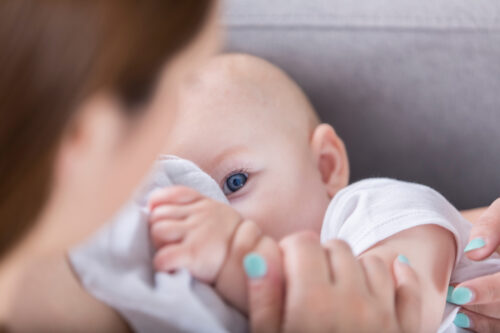 Close-up of a baby nursing and holding a blanket, representing the bonding and emotional complexity of breastfeeding experiences.