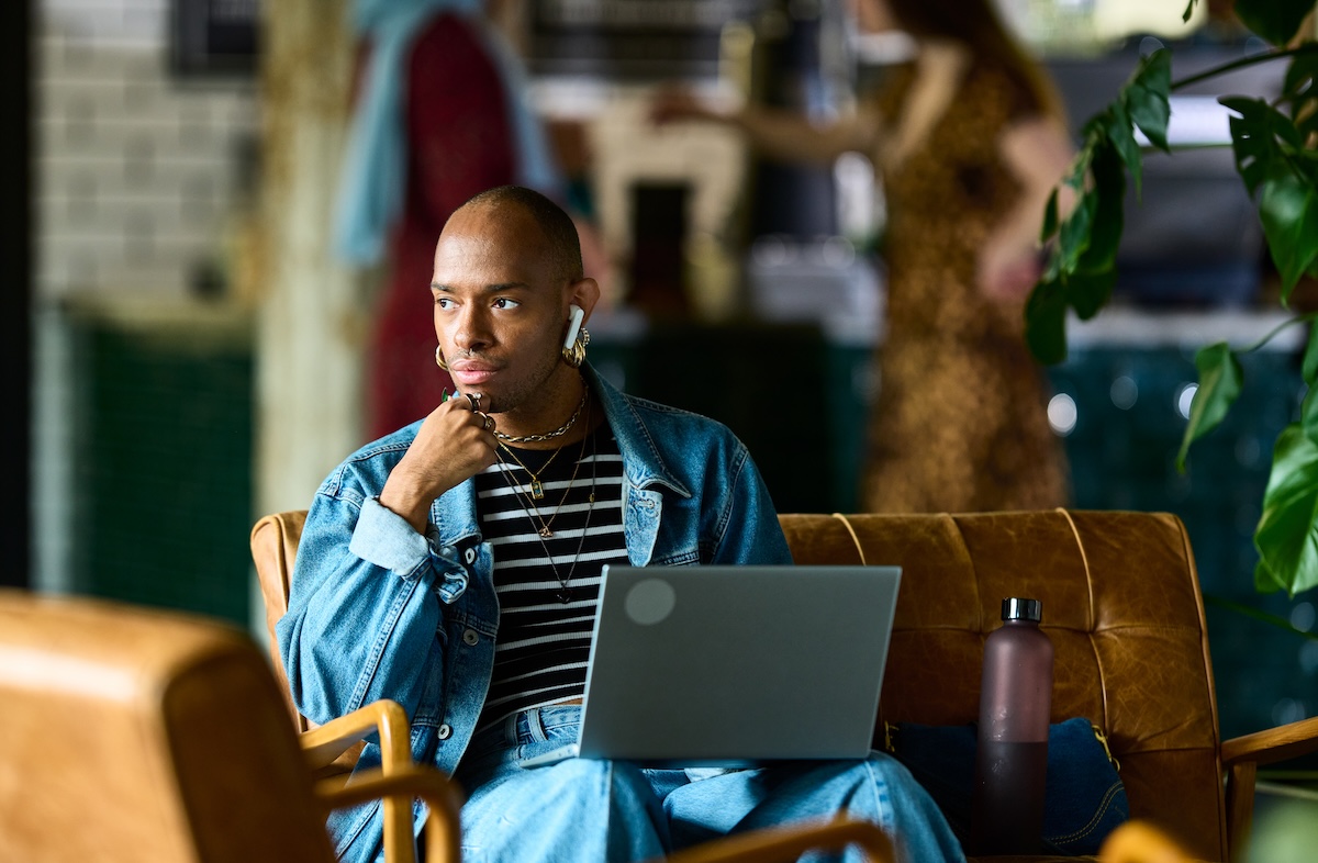Person sitting on couch and holding laptop, looking pensive.