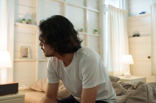 Man sitting on the edge of his bed with a troubled expression, illustrating the impact of substance use disorder before treatment placement.