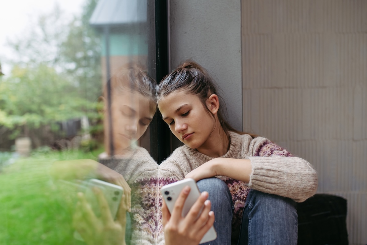 Teenage student looking at her phone, anxious and struggling with mental health.