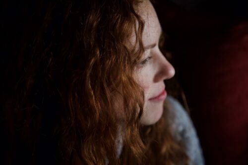 Woman with red hair looking off to the side, contemplative with a subtle smile.