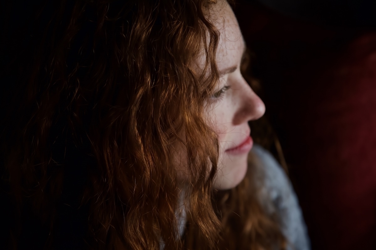 Woman with red hair looking off to the side, contemplative with a subtle smile.