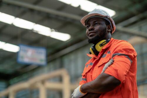Male engineer standing in a factory setting with his arms crossed wearing safety gear, considering an IOP.