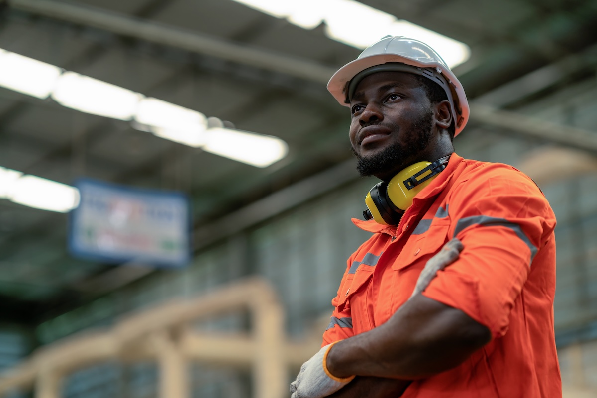 Male engineer standing in a factory setting with his arms crossed wearing safety gear, considering an IOP.