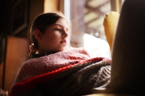 Young girl sitting in the sunlight, looking down to the side.