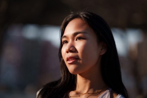 A teen girl, standing in the sun, looking off to the distance, feeling hopeful.