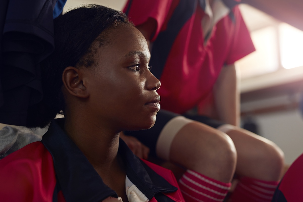 A teen girl sitting at school with classmates in the background.